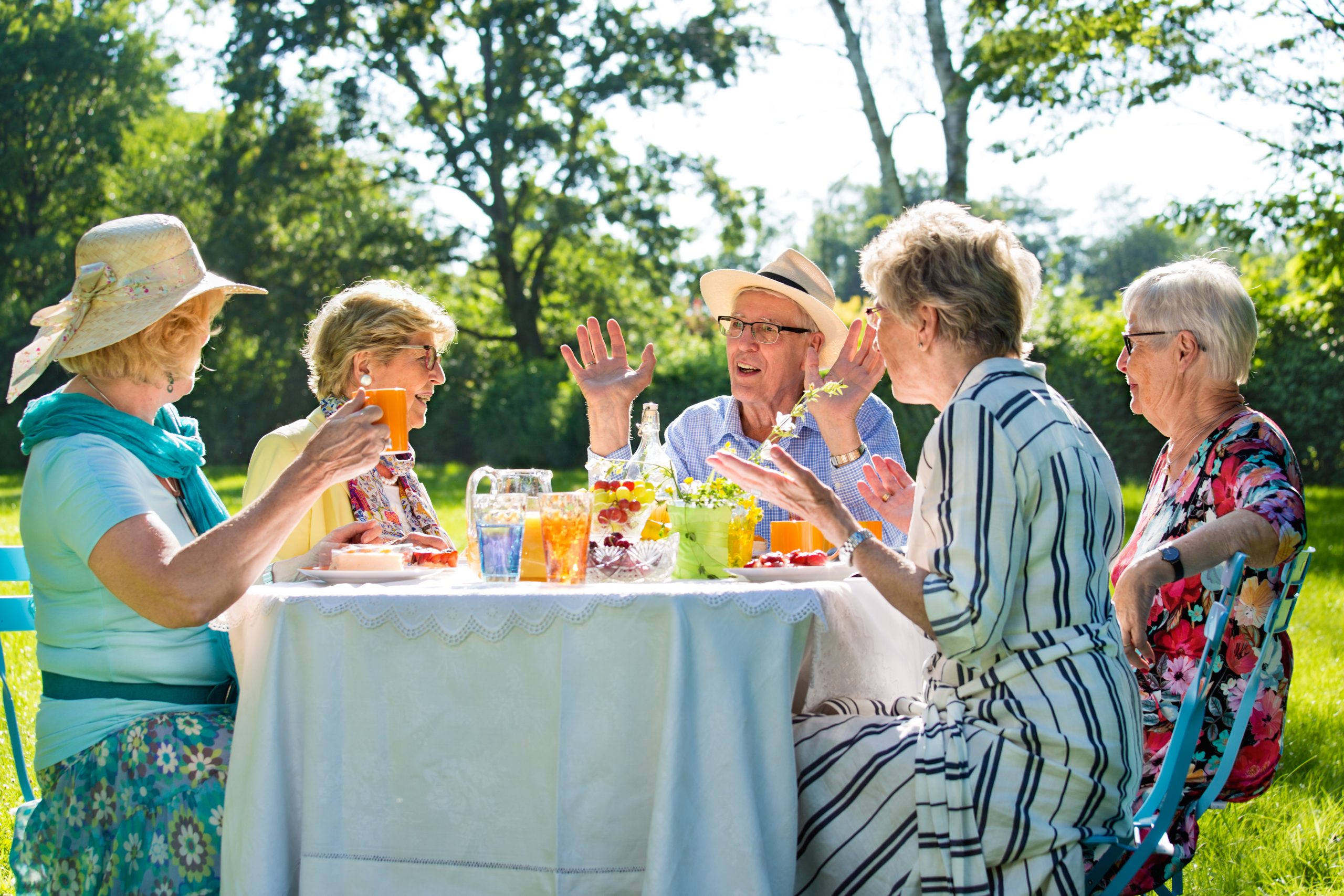 Senior friends having picnic with coffee and cake outdoors in sunshine.
